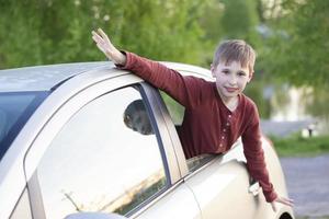 el pequeño chico atascado su cabeza fuera de el coche ventana. el niño se sienta en el coche y mira fuera el ventana vaso foto