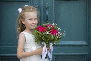 un linda pequeño niña es participación un ramo de flores de flores De las mujeres día. pequeño niña y flor. contento niño en fiesta con flores foto