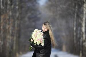 Beautiful middle-aged woman with a bouquet of white roses in the winter forest. photo