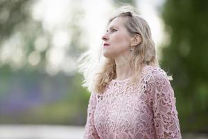 Beautiful elderly woman with long hair in profile.Romantic portrait of a beautiful elderly woman. Mature beautiful blonde in a pink dress. photo