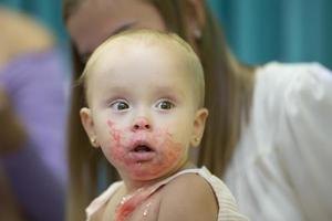 el pequeño niña manchado su cara con rosado dulce crema. foto