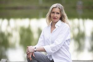 A beautiful middle-aged European woman. Fifty-year-old blonde woman in a white shirt on the background of nature. photo