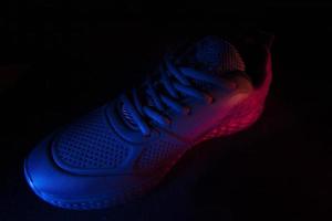 On a black background, sneakers illuminated by blue and red light filters. Beautiful sports shoes. photo