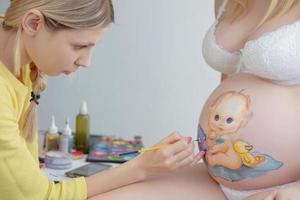 Makeup artist paints a cute baby on the belly photo