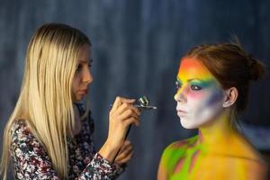 The artist puts a face painting on a beautiful young model photo