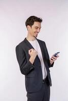 Portrait of a happy businessman using smartphone and doing winner gesture clenching fist over white background photo