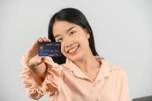 retrato de una joven asiática positiva que muestra un salario de buen humor con tarjeta de crédito aislado de fondo blanco foto