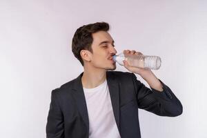 retrato de un joven feliz bebiendo agua de una botella y mirando una cámara aislada sobre fondo blanco foto