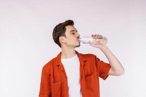 Portrait of Happy young man drinking water from a bottle and looking at camera isolated over white background photo