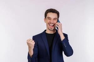 Portrait of happy handsome businessman talking by mobile phone and doing winner gesture clenching fist isolated over white background photo