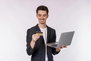 Portrait of young handsome smiling businessman holding creadit card and laptop in hands, typing and browsing web pages isolated on white background photo