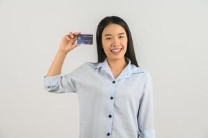 retrato de una joven asiática positiva que muestra un salario de buen humor con tarjeta de crédito aislado de fondo blanco foto
