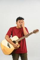 retrato de un joven asiático con una camiseta roja con una guitarra acústica aislada de fondo blanco foto