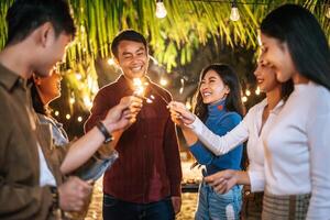 retrato de feliz grupo asiático de amigos divirtiéndose con bengalas al aire libre - jóvenes divirtiéndose con fuegos artificiales en la noche - gente, comida, estilo de vida de bebida, concepto de celebración de año nuevo. foto