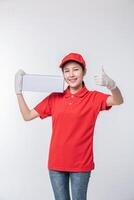 Image of  young delivery man in red cap blank t-shirt uniform standing with empty white cardboard box isolated on light gray background studio photo