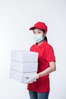 Image of a conscious young delivery man in red cap blank t-shirt uniform face mask gloves standing with empty white cardboard box isolated on light gray background studio photo