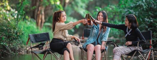 mujeres jóvenes sentadas y bebiendo bebidas mientras acampan en el bosque foto