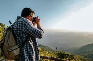 el joven mochilero usa la cámara para tomar fotos en el bosque.