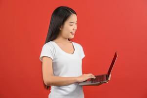 Portrait of a happy asian businesswoman working on laptop computer isolated over red background photo