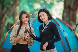 Young women cheer and drink beverage  front of camping tent photo