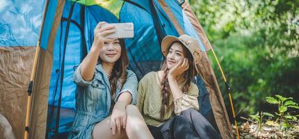 Asian pretty woman and friend use smartphone selfie on camping photo