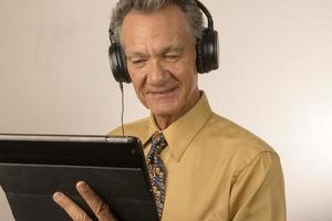 Older Man listening to music or a podcast wearing head phone on his smart tablet photo