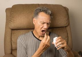 Older man sitting in an EZ chair taking his medication photo