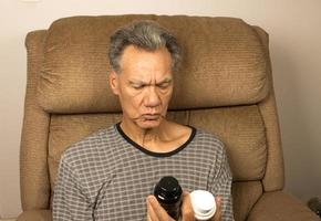 Older man sitting in an EZ chair reading the label on his medicine bottle photo