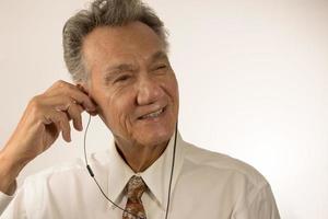 más viejo hombre escuchando a música o un podcast utilizando oído brotes en su teléfono inteligente foto