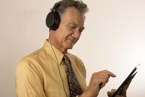 Older Man listening to music or a podcast wearing head phone on his smart tablet photo