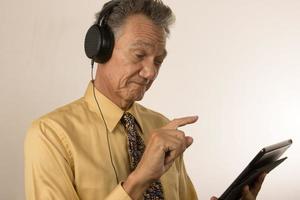 Older Man listening to music or a podcast wearing head phone on his smart tablet photo