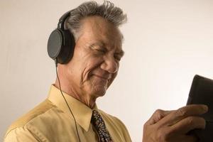 más viejo hombre escuchando a música o un podcast vistiendo cabeza teléfono en su inteligente tableta foto