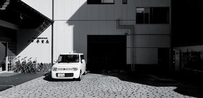 Japan-February 2, 2023 White modern car parked in front of hotel entrance in black and white or monochrome tone. Vehicle with building background and shadow. photo