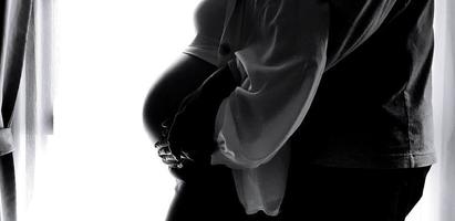 Silhouette of Close up husband's hand hug and touching wife's belly with white curtain background and left copy space in black and white tone. Pregnant, New life and Lover family in monochrome style. photo
