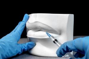 Close up hands of a cosmetologist making botox injections in plaster white female lips. Creative lip injection photo