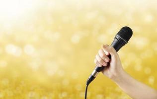 Female hand with microphone on golden background photo