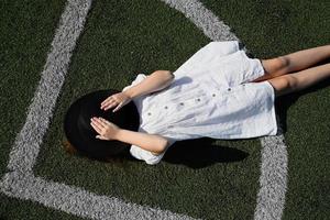 A girl in a hat, lying in the stadium. Active recreation in a white dress