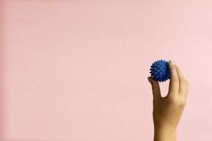 Womans hand with Spiny plastic blue massage ball on pink background photo