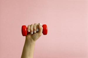 Womans hand with red dumbbells on pink background photo