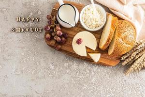 the spring holiday of the Jews of Shavuot. a festive card with traditional food and ears of corn. wooden letters on a grey background - happy shavuot. photo