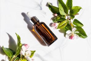 a bottle with a cosmetic or serum for the care of the skin of the face on a marble white background and twigs of a flowering apple tree. top view. photo