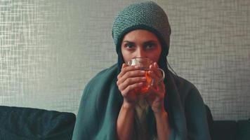 Caucasian resilient woman sits under blanket on sofa with cup of tea look at camera. Rising costs in private households for gas bill due to inflation and war, Energy crisis video