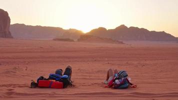 Jordanië, 2022 - jong Kaukasisch paar leggen kom tot rust Aan zand samen houden hand- in liefde kijk maar zonsondergang in woestijn buitenshuis in wadi rum buitenshuis in Jordanië. reizen onderzoeken saamhorigheid in moslim land video