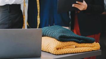 Moda diseñador l joven asiático mujer trabajando utilizando computadora portátil, tableta y sonriente mientras en pie en taller respondiendo en negocio video