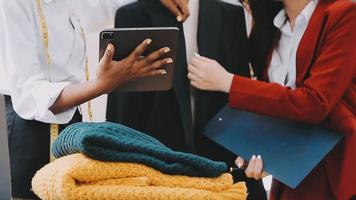 moda progettista l giovane asiatico donna Lavorando utilizzando computer portatile, tavoletta e sorridente mentre in piedi nel laboratorio rispondere su attività commerciale video