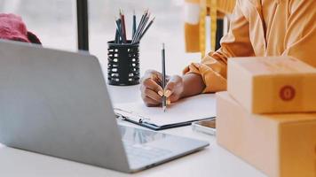 Moda diseñador l joven asiático mujer trabajando utilizando computadora portátil, tableta y sonriente mientras en pie en taller respondiendo en negocio video