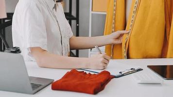 Calm curly brunette dark skinned woman on desk in office of fashion designer and holds tablet and smartphone video