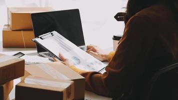 Calm curly brunette dark skinned woman on desk in office of fashion designer and holds tablet and smartphone video