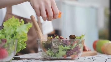 Young and happy woman eating healthy salad sitting on the table with green fresh ingredients indoors video