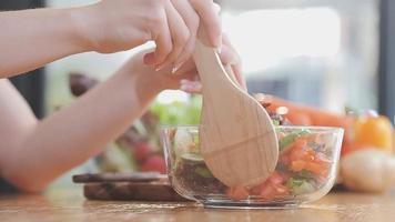 Young and happy woman eating healthy salad sitting on the table with green fresh ingredients indoors video